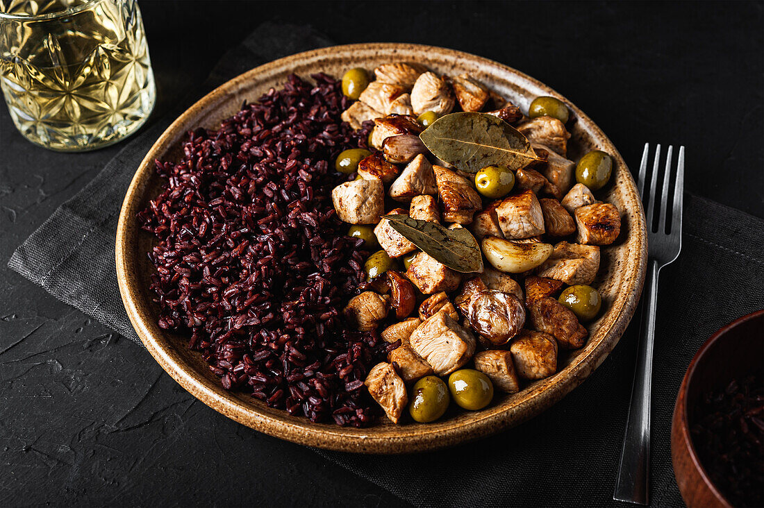 Von oben gesehen runder Teller mit schmackhaftem sautiertem Truthahn mit Oliven neben einem Glas Getränk auf einem schwarzen Tisch im Restaurant