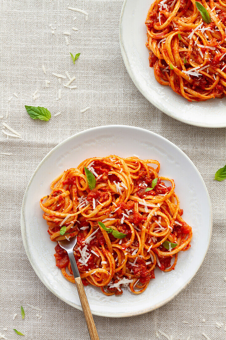 Blick von oben auf appetitliche hausgemachte Pasta mit Bolognesesoße, serviert mit frischen Basilikumblättern auf einem weißen Teller