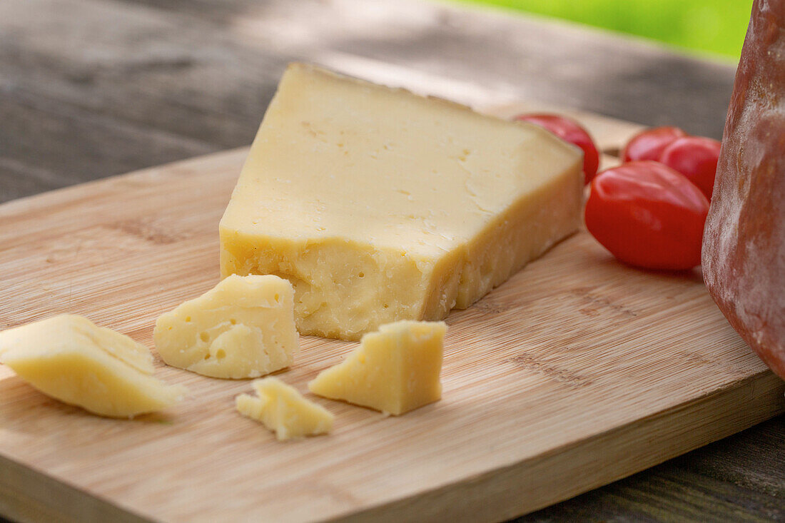 Köstlicher italienischer Pecorino toscano-Käse mit Kirschtomaten auf einem Schneidebrett auf einem Holztisch im Garten