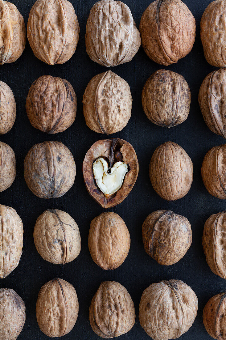 Top view of textured backdrop representing heart shaped walnut center among whole nuts with uneven nutshells