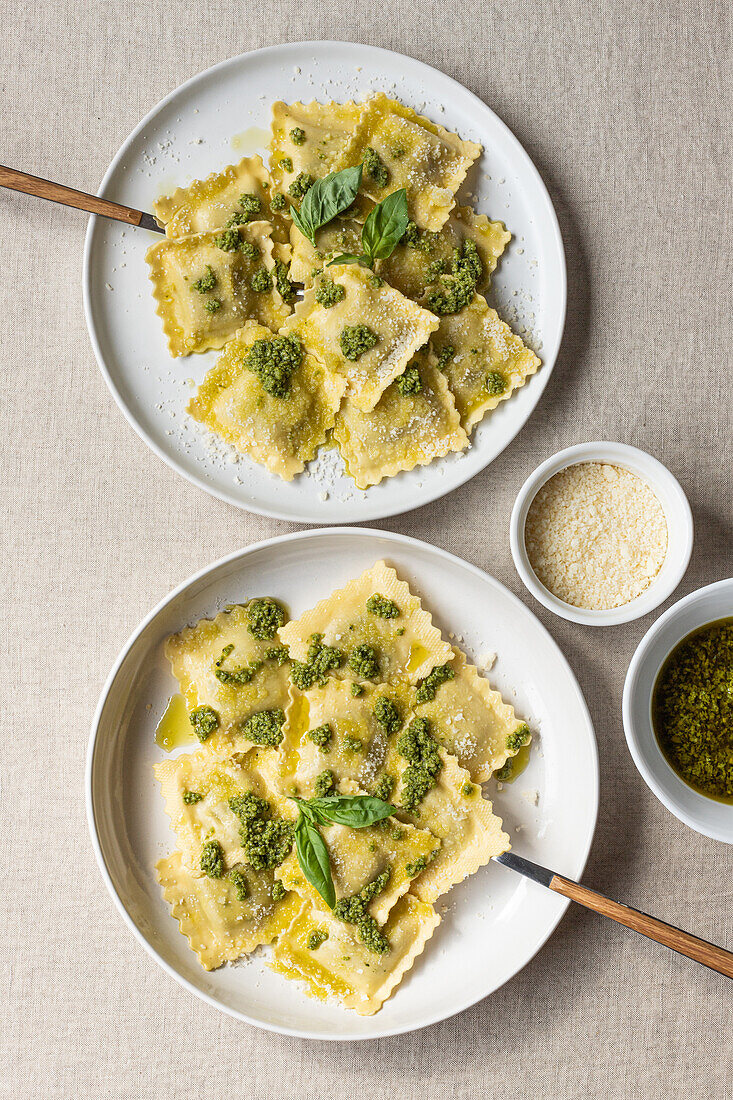 Draufsicht auf appetitlich gekochte Ravioli mit grüner Soße und Kräutern auf weißen Tellern mit Gabeln auf dem Tisch