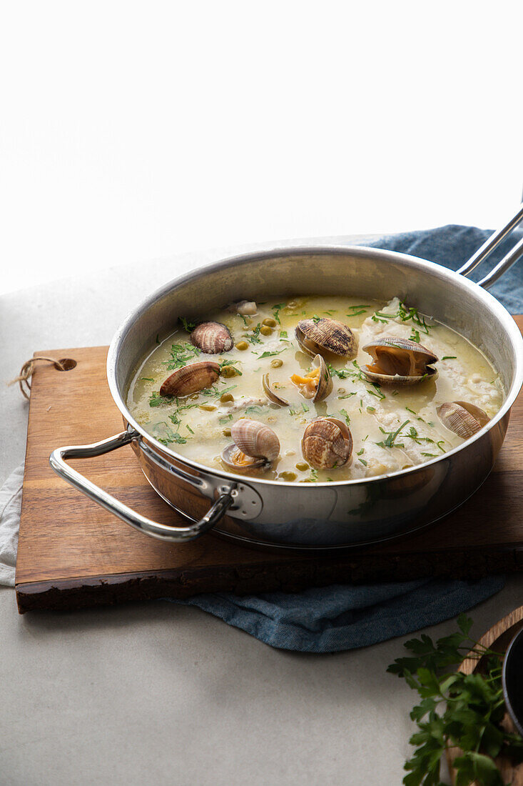 Draufsicht von oben auf einen Metalltopf mit leckerer Meeresfrüchtesuppe mit Muscheln und Seehecht auf einem Holzbrett in der Küche