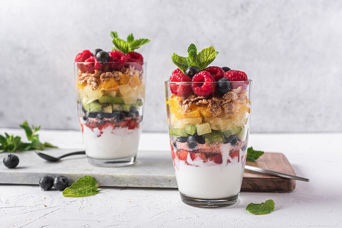 Appetitlicher Joghurt mit Schichten von frischen Früchten, serviert in Gläsern auf einem Tisch mit Minzblättern