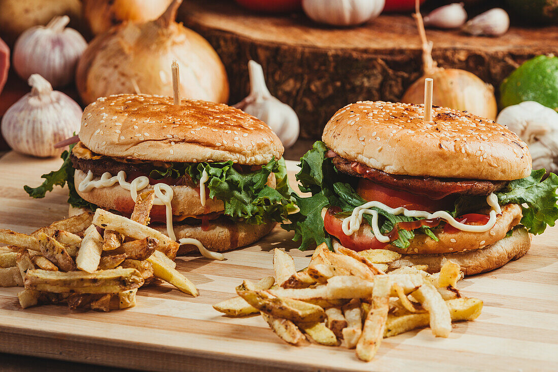 Appetitliche Hamburger mit Gemüse und Schnitzel auf einem Holzbrett mit Pommes frites in der Küche