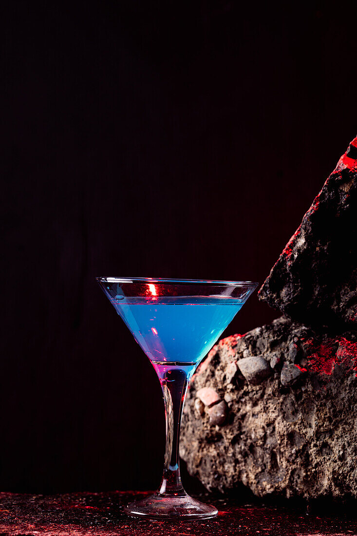 Blaue-Lagune-Cocktail in elegantem Kristallglas auf rauer Oberfläche vor schwarzem Hintergrund