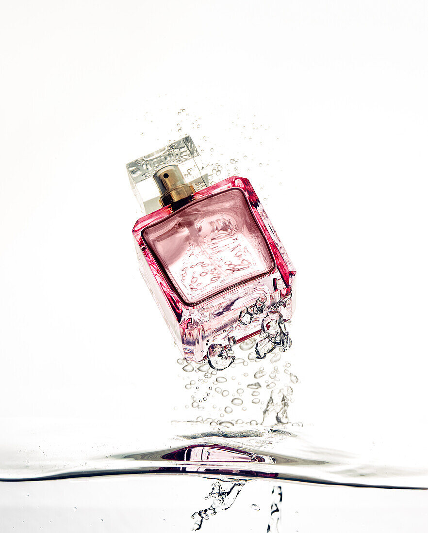Kreatives Design eines Flakons mit aromatischem Parfüm zwischen spritzenden Flüssigkeitstropfen und Luftblasen