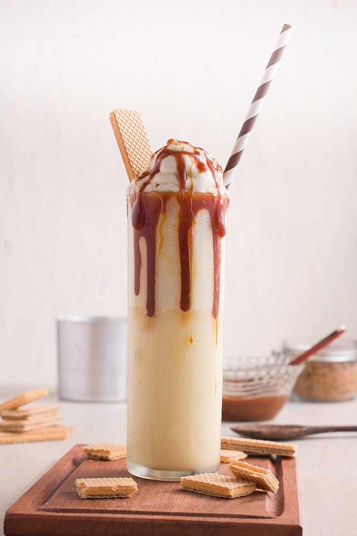 Glas mit süßem Karamellmilchshake mit Vanilleeis und Waffelkeksen auf dem Tisch