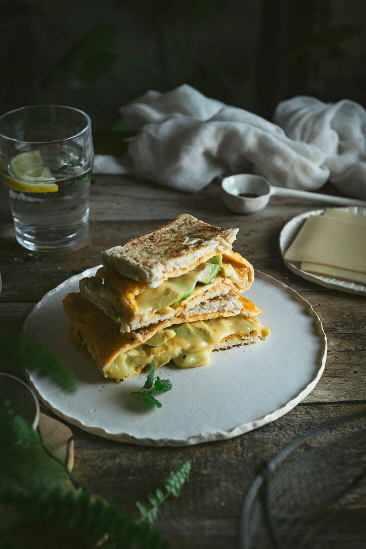 Avocado, Käse, Omelett-Sandwich auf Keramikteller auf Holztisch serviert