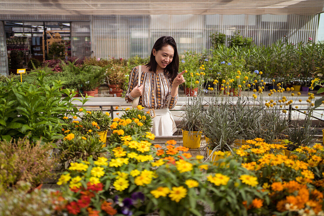 Fröhliche junge ethnische Käuferin lehnt sich nach vorne und pflückt blühende Blumen in einem Gartencenter