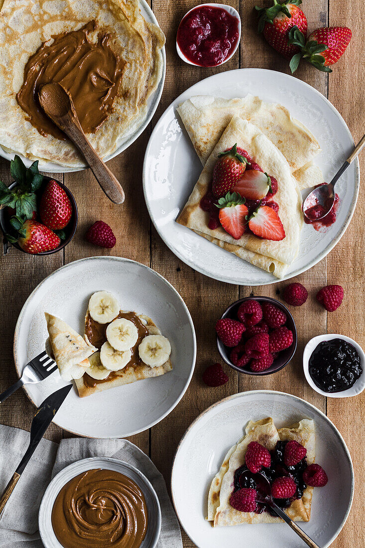 Von oben Teller mit leckeren Crêpes mit verschiedenen Belägen, die beim Frühstück auf einem Holztisch stehen