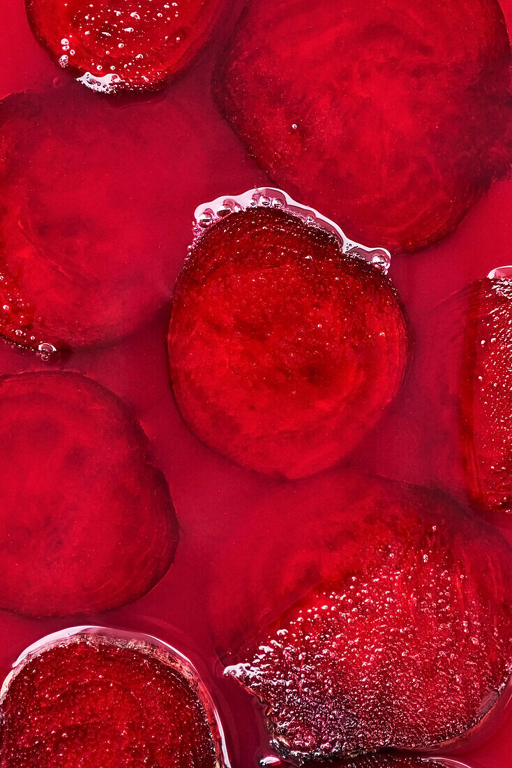 Scheiben geschnittener frischer roter Beete auf nasser heller fuchsiafarbener Oberfläche als abstrakter Hintergrund