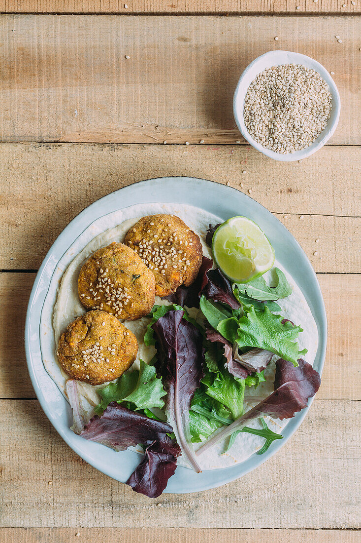 Blick von oben auf einen Teller mit Süßkartoffel-Falafel und Salat mit Limette auf einem Holztisch