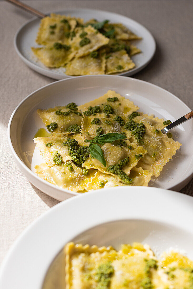 Appetitlich gekochte Ravioli Nudeln mit grüner Soße und Kräutern auf weißen Tellern mit Gabeln auf dem Tisch