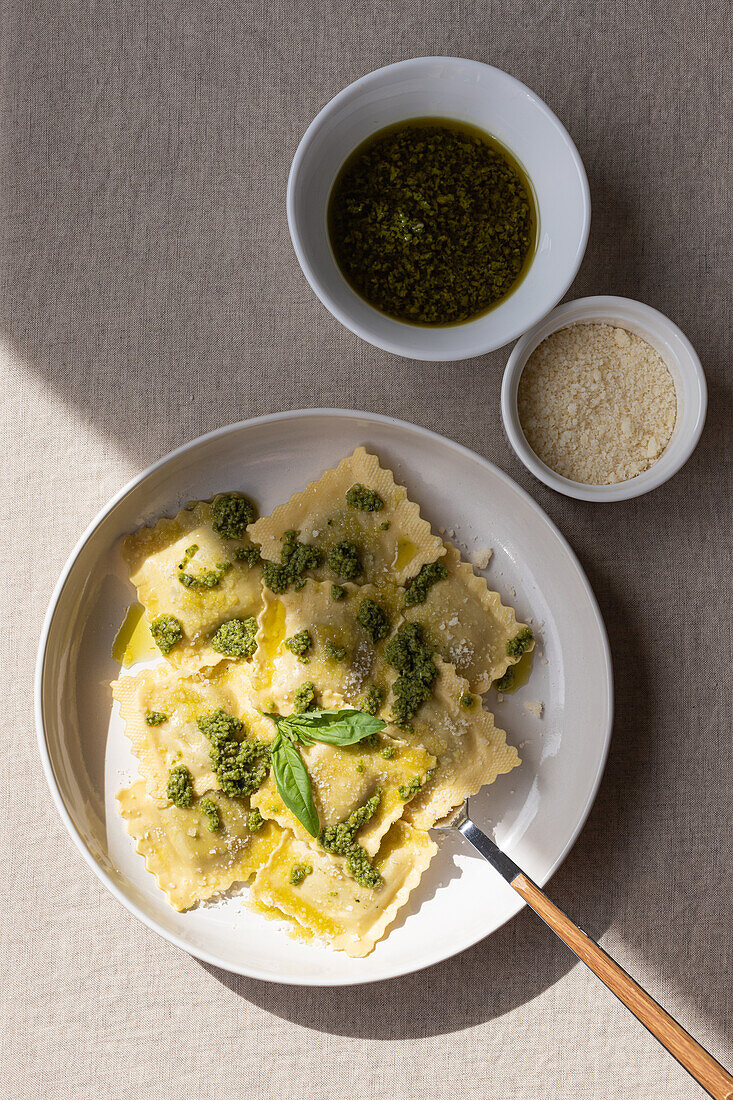 Draufsicht auf appetitliche gekochte Ravioli mit grüner Soße und Kräutern auf weißem Teller mit Gabel auf dem Tisch