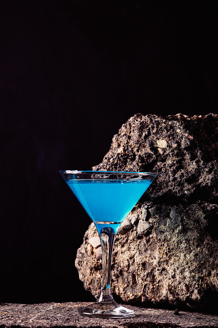 Blaue-Lagune-Cocktail in elegantem Kristallglas auf rauer Oberfläche vor schwarzem Hintergrund