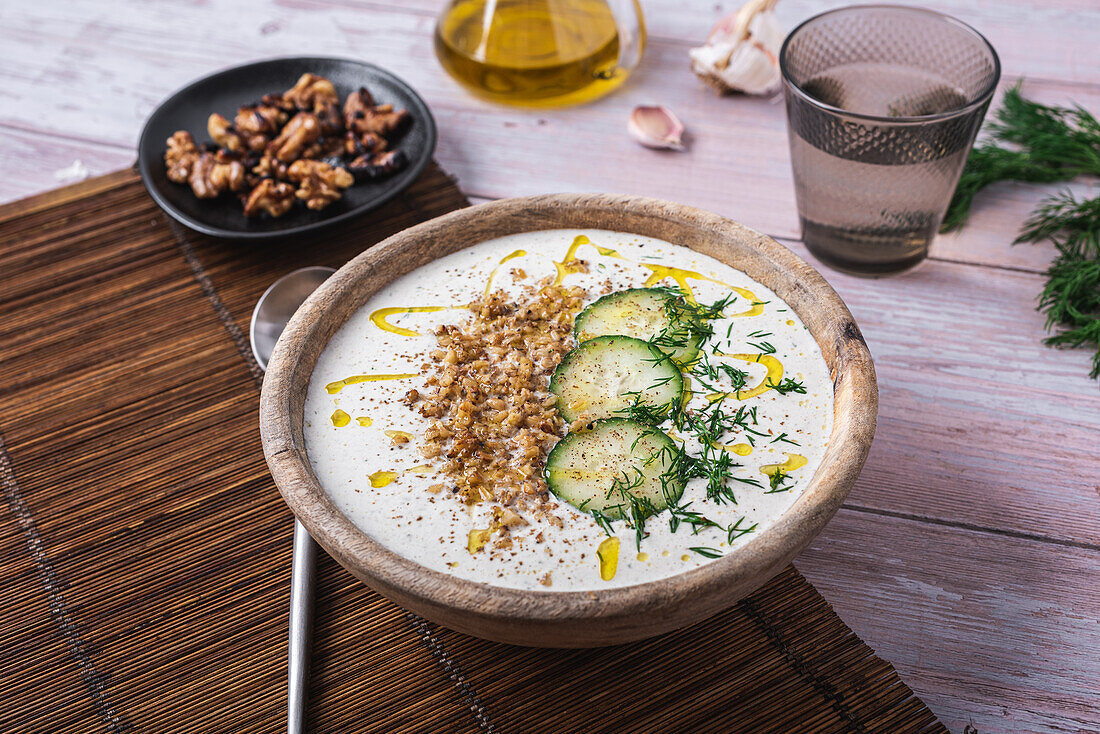 Schüssel mit traditioneller bulgarischer kalter Sommersuppe Tarator mit Joghurt neben einem Glas Wasser und einem Teller mit Nüssen von oben