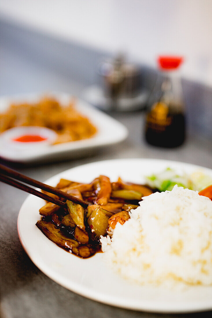 Appetitlich gekochte Yuxiang-Aubergine mit gesundem Gemüse und Reis auf weißem Teller in asiatischem Restaurant