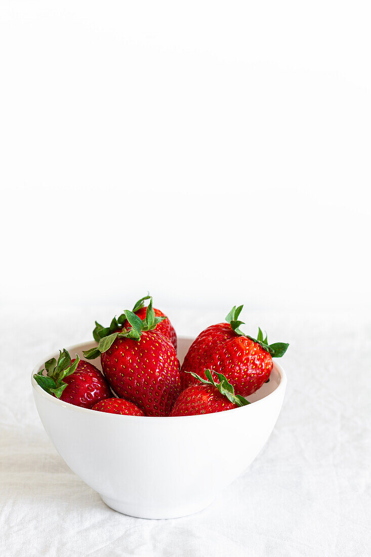 Leckere frische Erdbeeren mit Kelchblättern in einer runden Schale auf zerknittertem Stoff auf schwarzem Hintergrund