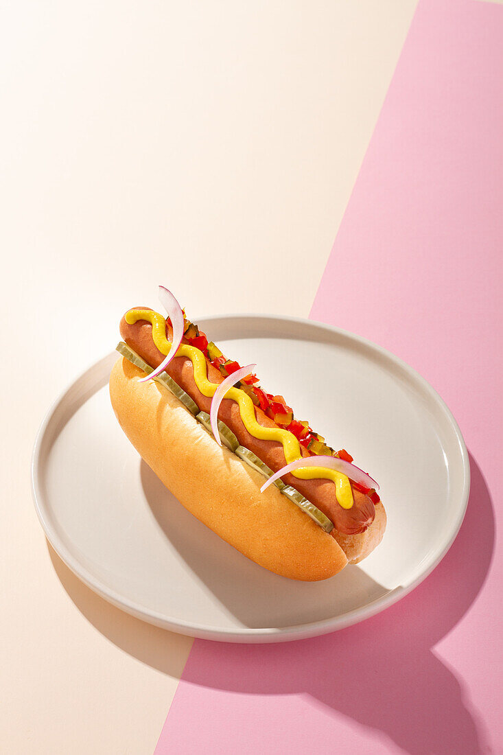 From above an appetizing hot dog in a round plate on a white and pink background