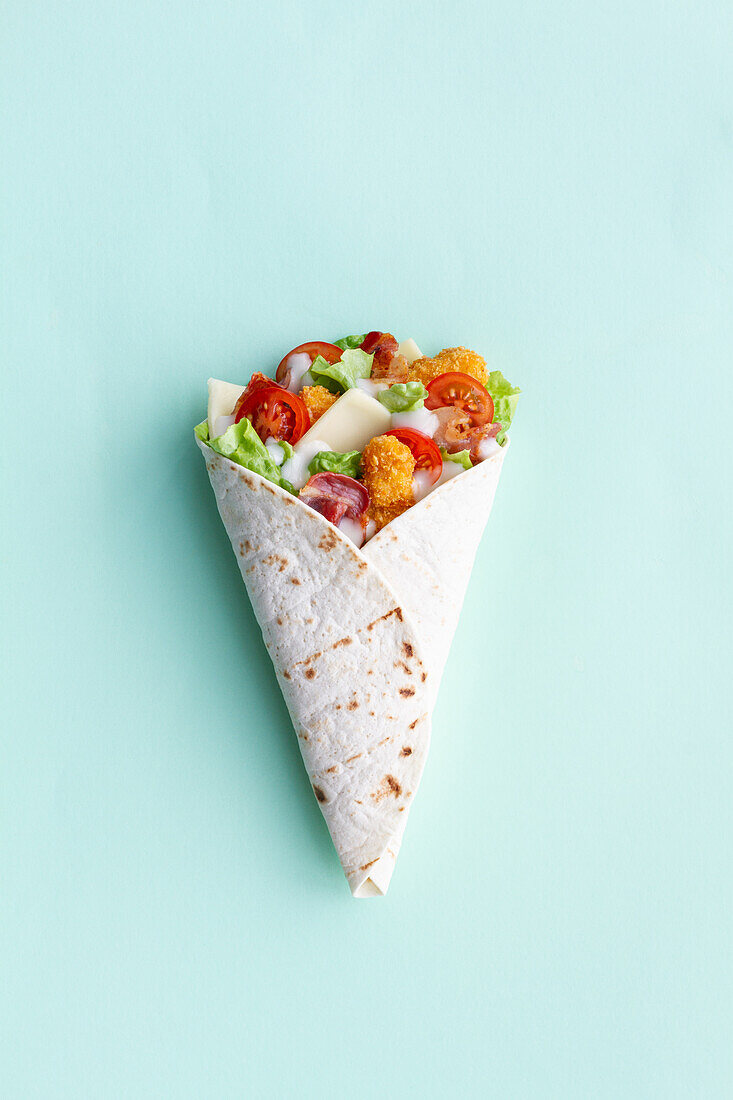 Top view of delicious chicken wrap with fresh lettuce and ripe tomatoes in tortilla placed on light background in studio