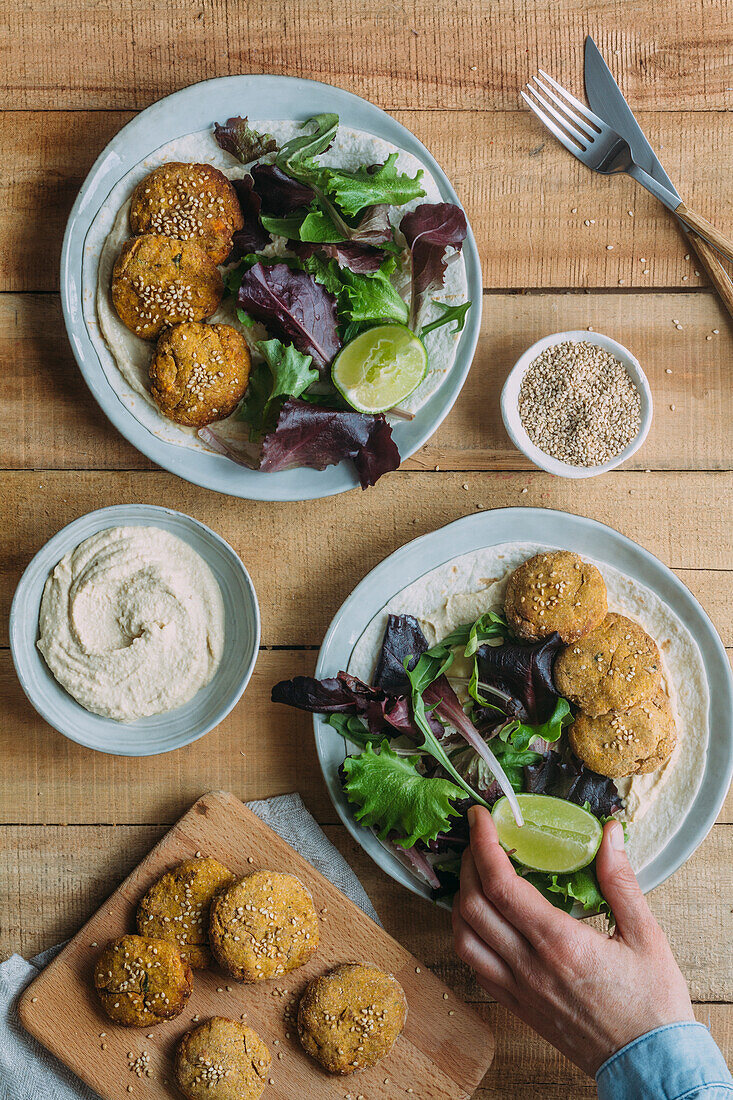 Teller mit frischem Salat und Süßkartoffel-Falafel neben Soße und Sesam auf Holztisch