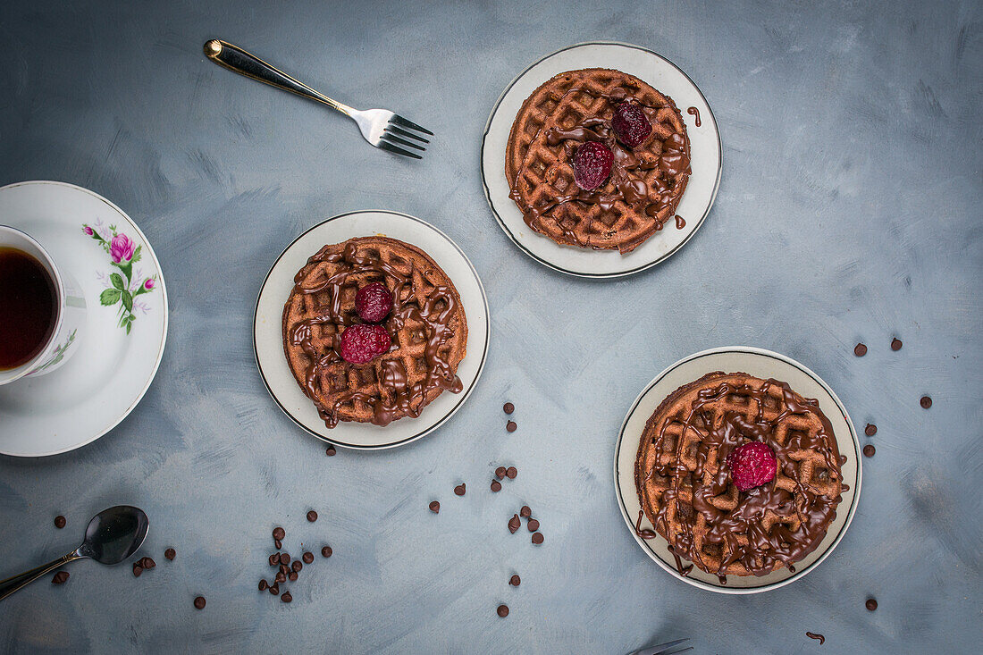 Von oben: leckere süße Waffeln mit Schokoladensauce und Himbeeren, serviert auf einem Tisch mit Schokoladendrops in einer hellen Küche