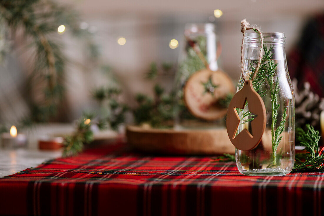 Weihnachtlich gedeckter Tisch mit Kranz und dekorativen Holzornamenten und rot karierter Tischdecke mit gelben Lichtern im Hintergrund