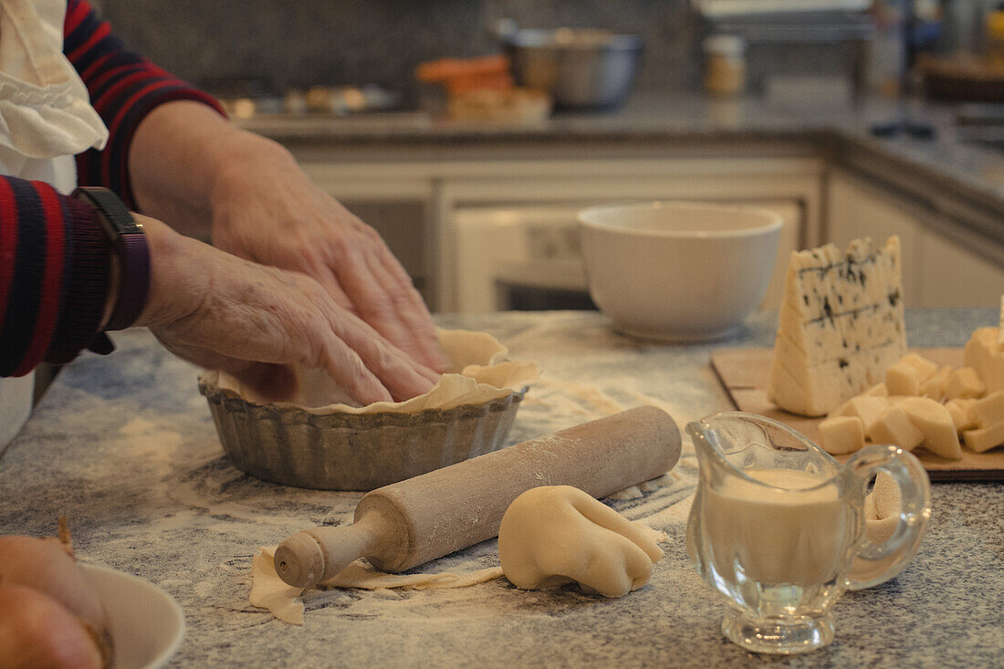 Anonyme Köchin mit Gebäckkruste über einem Tisch mit Backform und verschiedenen Käsesorten während des Backvorgangs