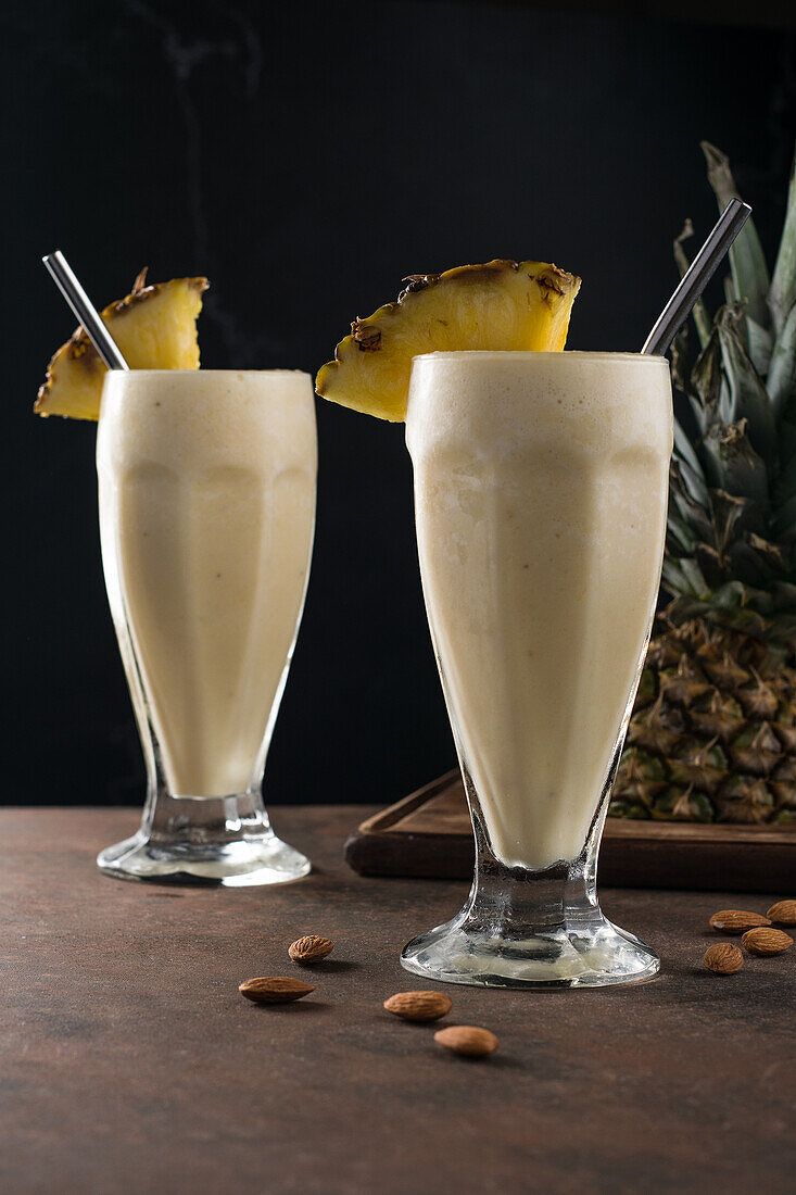 Sweet refreshing cold pina colada smoothie served with pineapple slices on table with scattered almond