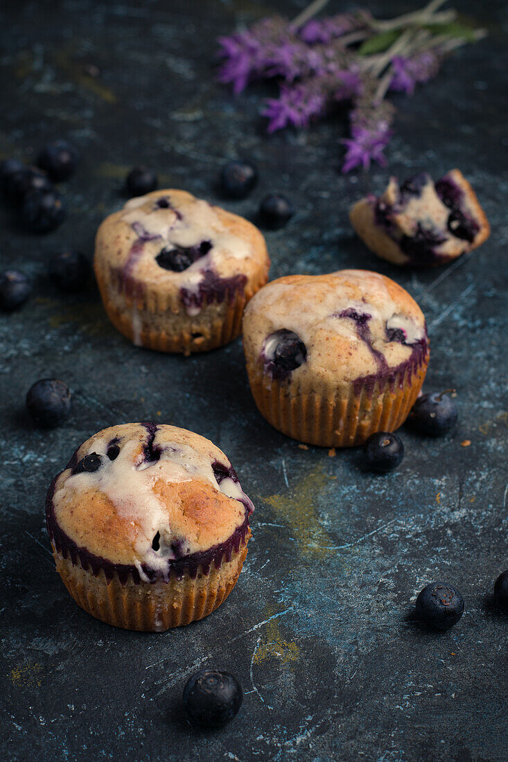 Hoher Winkel von süßen hausgemachten Muffins mit Sahne und Blaubeeren in der Nähe von Blumen auf dem Tisch