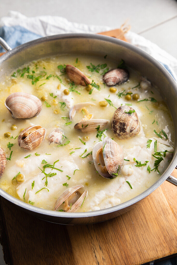 Draufsicht von oben auf einen Metalltopf mit leckerer Meeresfrüchtesuppe mit Muscheln und Seehecht auf einem Holzbrett in der Küche