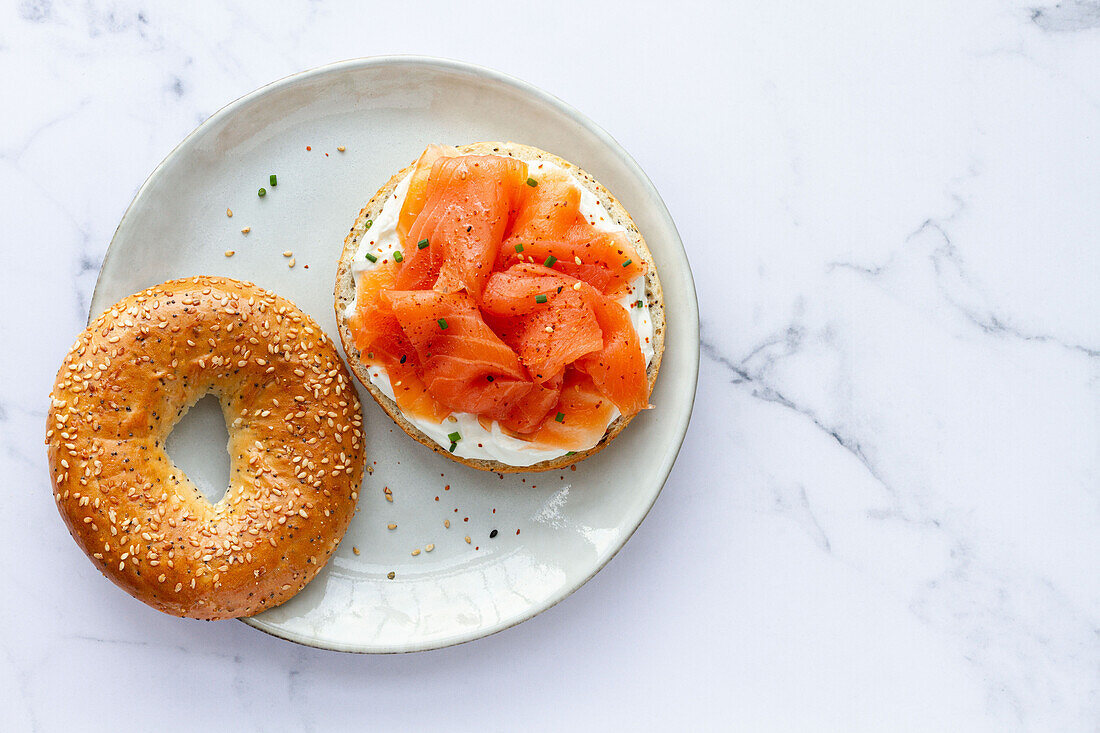 Von oben frischer Bagel mit Käse und Lachs auf einem Teller, serviert auf einem Tisch mit einer Tasse heißem Kaffee in einer hellen Küche