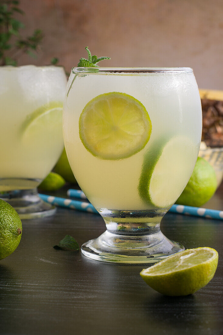 Cold cocktails consisting of lime pieces ice cubed and mint leaves served with bowl of chopped pineapple