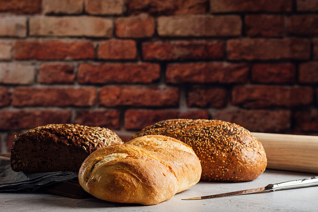 Weiß- und Roggenbrot mit Getreide und appetitlicher Kruste auf einem Schneidebrett vor einer Backsteinwand in einer Backstube