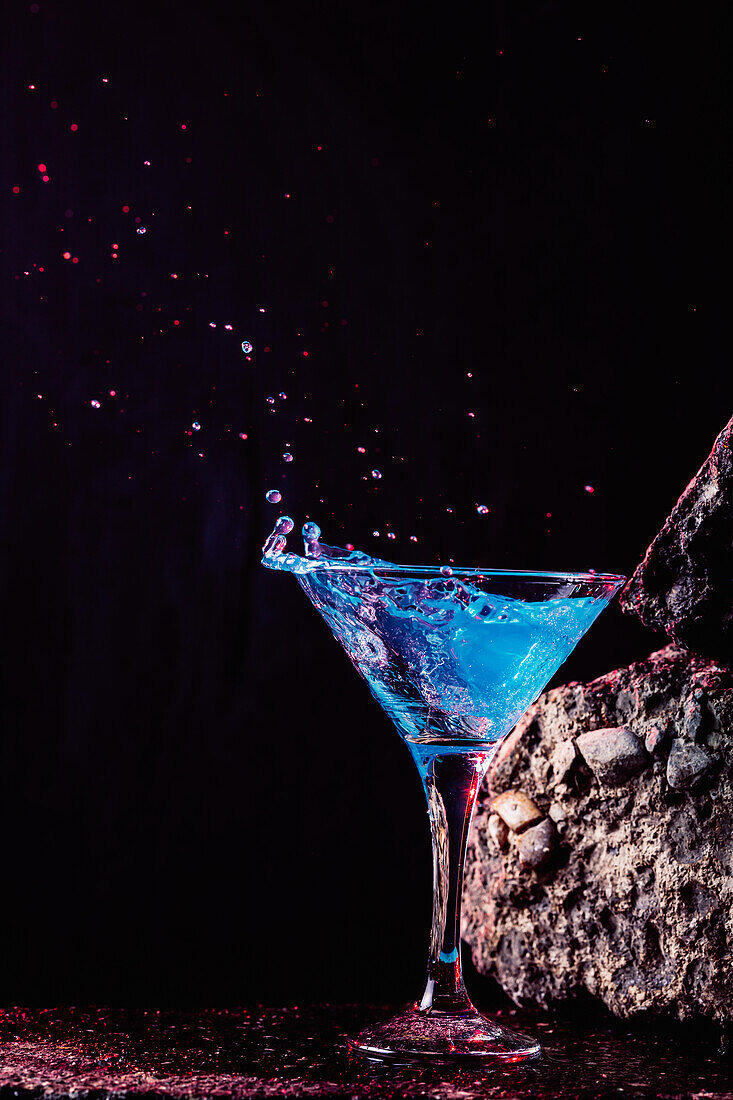 Blaue-Lagune-Cocktail in elegantem Kristallglas auf rauer Oberfläche vor schwarzem Hintergrund