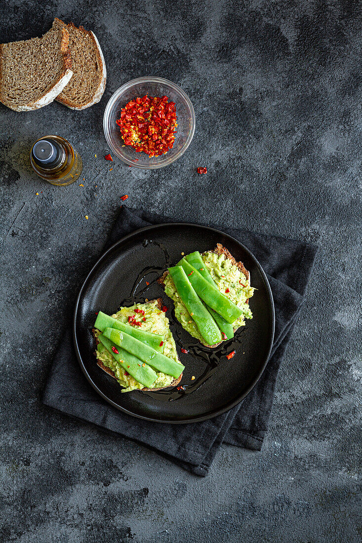 Appetitliche Toasts mit frischer Guacamole und grünen Erbsenschoten, garniert mit rotem Paprika und serviert auf einem schwarzen Teller