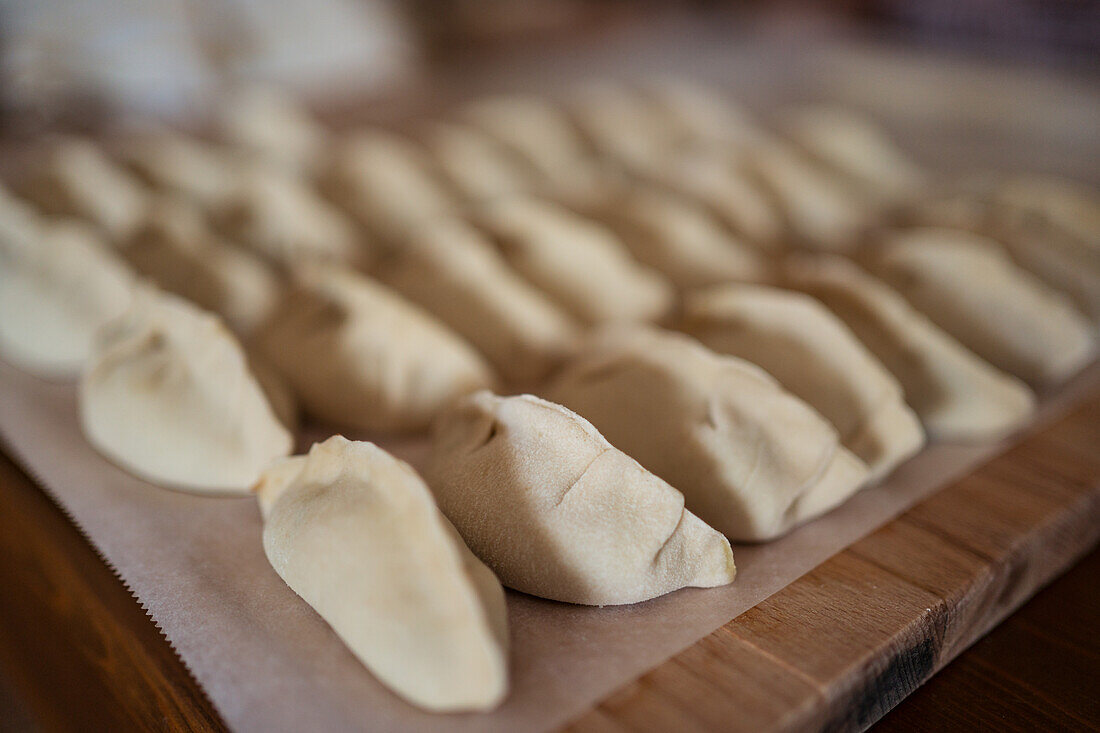 Nahaufnahme von gefüllten, ungekochten Jiaozi-Knödeln, die auf einem Holztisch in einer Reihe in der Küche serviert werden