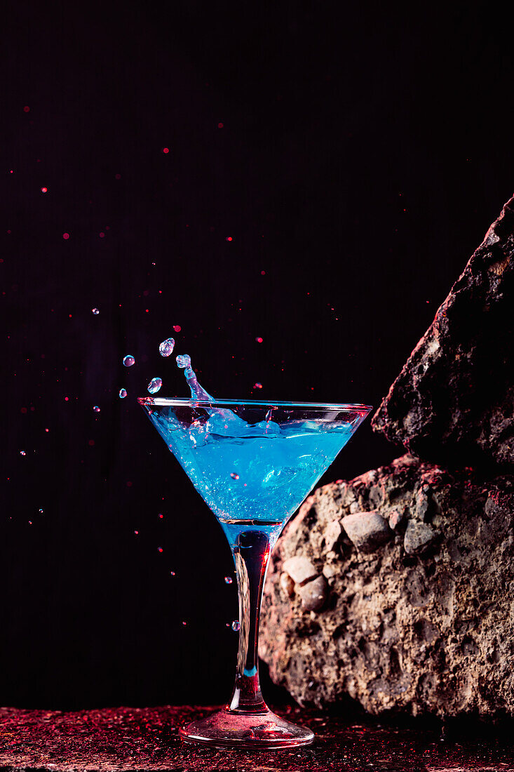 Blaue-Lagune-Cocktail in elegantem Kristallglas auf rauer Oberfläche vor schwarzem Hintergrund