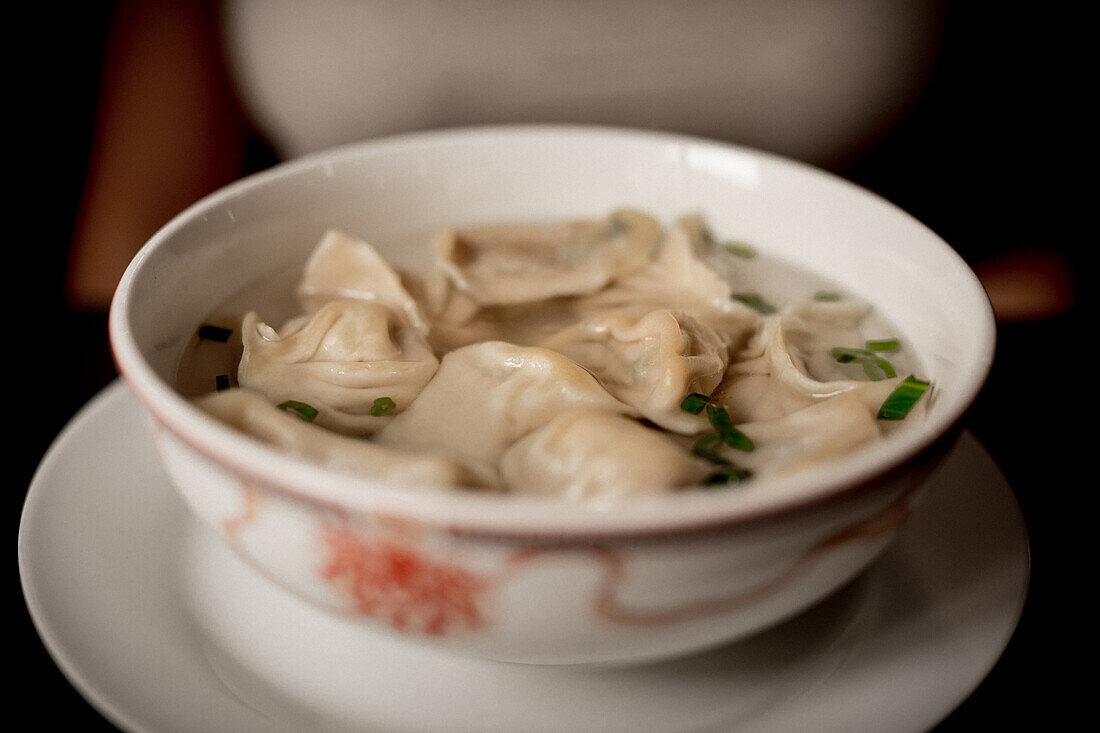 Closeup bowl of delicious soup with dumplings and spring onion against black background