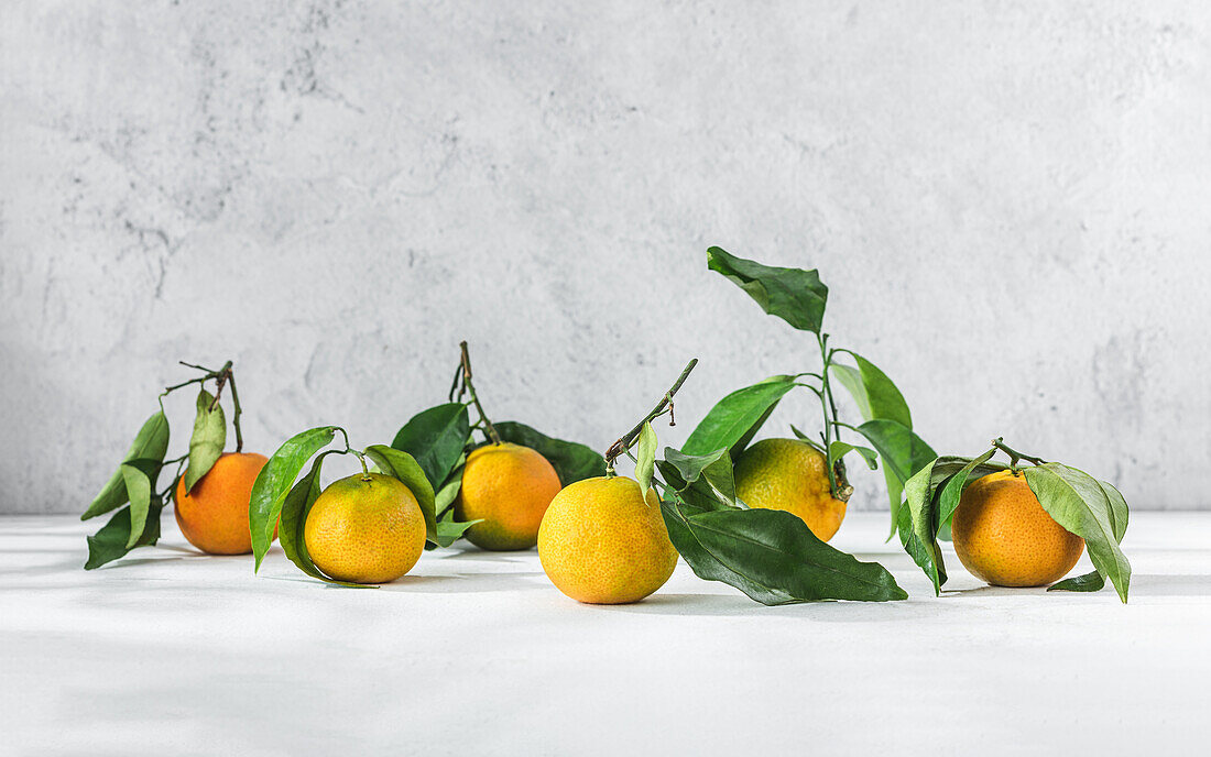 Orangefarbene Mandarinen mit grünem Stiel und Blatt liegen auf einem weißen Tisch