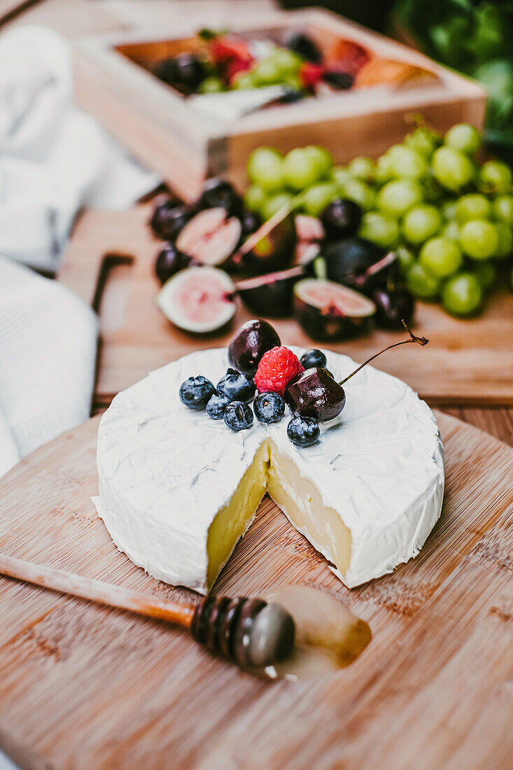 Frischer Camembert-Käse unter reifen Blaubeeren und Kirschen auf Holzbrett mit Honiglöffel