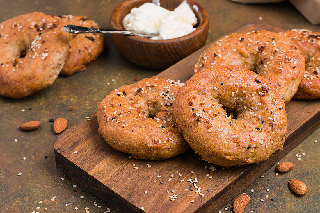 Leckere gebackene kohlenhydratarme Bagels auf einem Holzbrett auf einem Tisch mit Mandeln und Frischkäse in einer hellen Küche