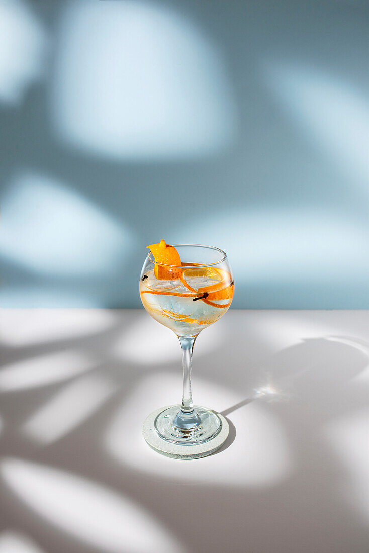 Transparentes Glas mit Highball-Cocktail, verziert mit Zitrusfruchtschalen und Nelken im Schatten des Sonnenlichts