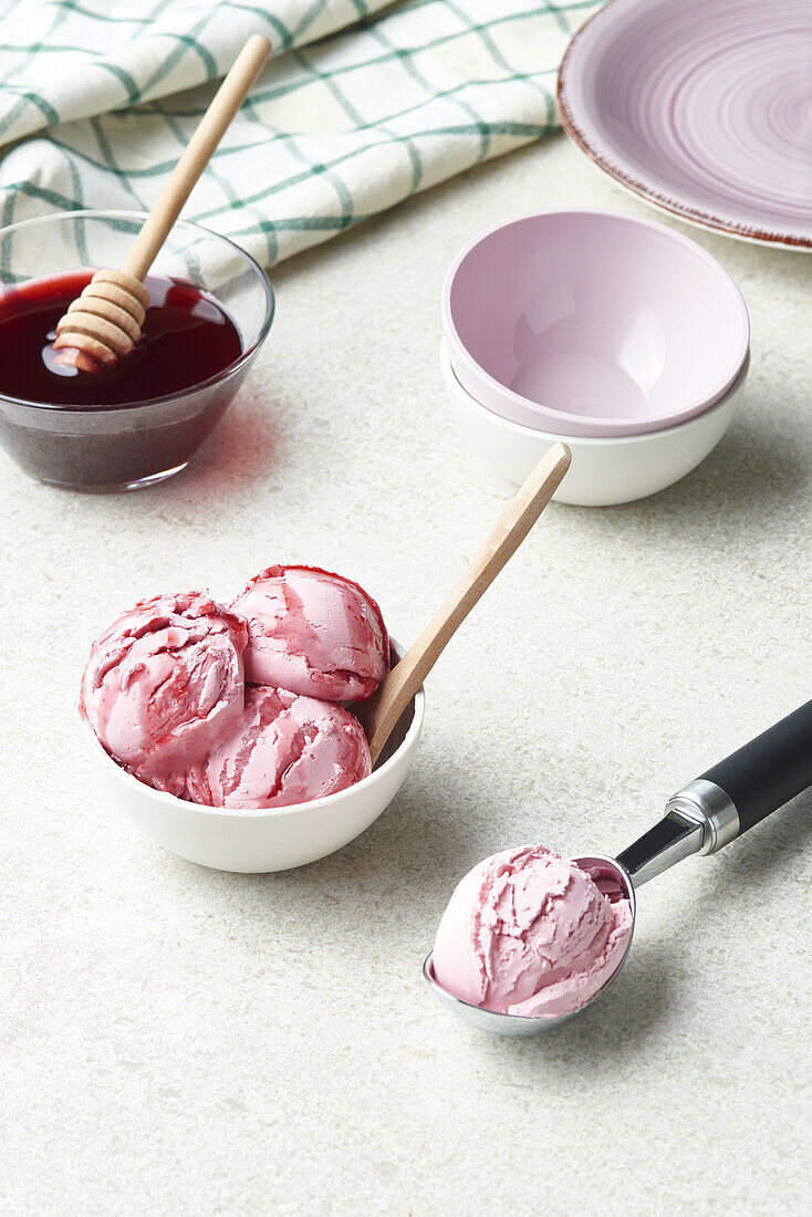 High angle of scoops of delicious homemade ice cream served in bowl and topped with berry syrup in light kitchen