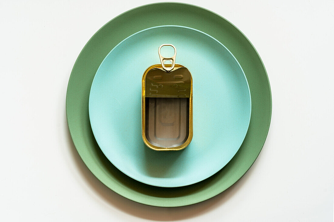 Top view of opened empty metal can with pop up lid placed on blue ceramic plate served on white table with silver fork and knife