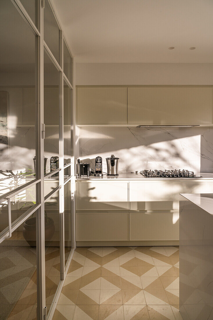 Interior of contemporary home kitchen with light furniture and mirrored elements in daylight