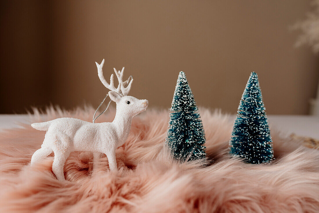 Von oben weihnachtlich gedeckter Tisch mit weißem Rentier auf flauschigem rosa Tischset neben blauem Tannenbaum