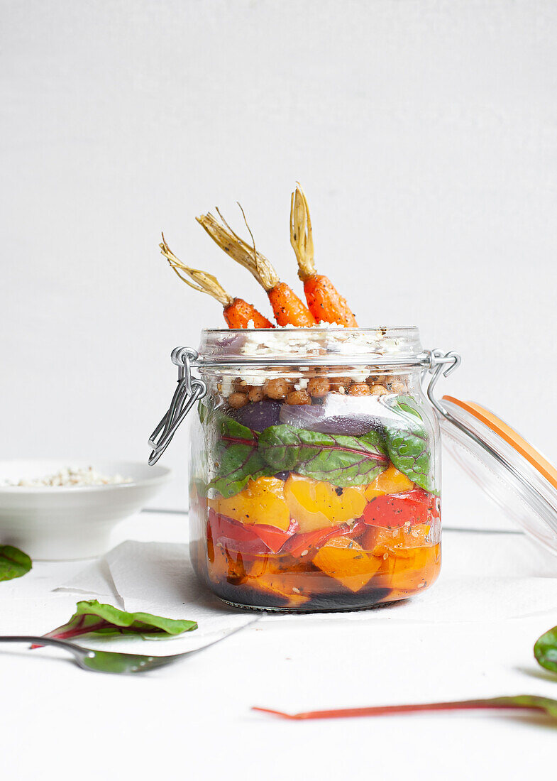 Salat mit bunten, reifen, gehackten Paprikaschoten und Bulgur mit rohen Karotten in einem Glas auf einem Tisch vor weißem Hintergrund