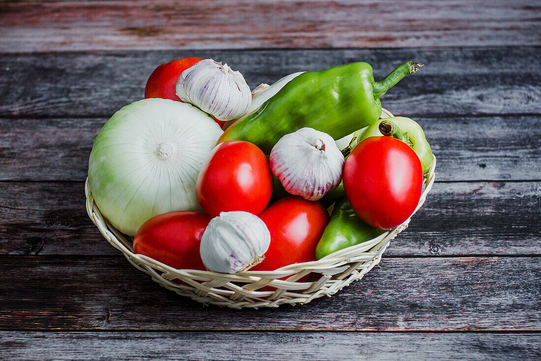 Frische reife Tomaten neben Paprika und Knoblauch in einer Schüssel auf einem Holztisch zu Hause