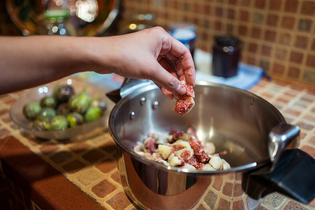Crop unrecognizable person putting fresh fig piece in pressure cooker in house kitchen on blurred background
